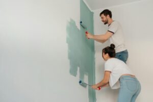 A young couple collaborates on painting a wall with rollers, highlighting teamwork and home improvement.